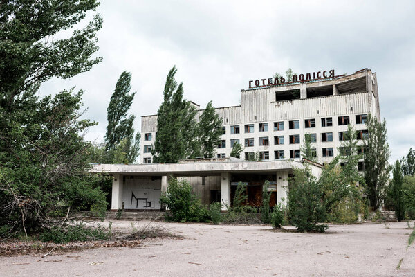 PRIPYAT, UKRAINE - AUGUST 15, 2019: building with hotel polissya lettering near trees in chernobyl 
