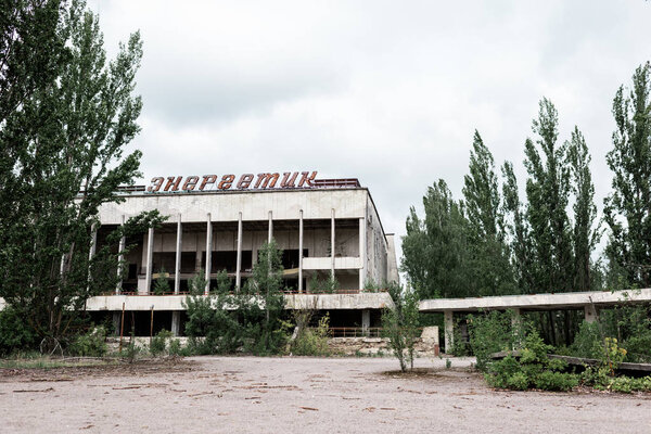 PRIPYAT, UKRAINE - AUGUST 15, 2019: building with energetic letters near green trees in chernobyl 