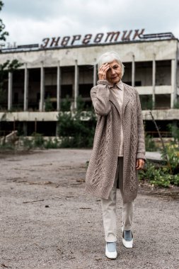 Pripyat, Ukrayna - 15 Ağustos 2019: Çernobil'de enerjik harflerle binanın yakınında yürüyen yaşlı kadın 