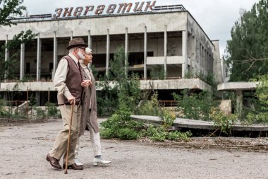 Pripyat, Ukrayna - 15 Ağustos 2019: Çernobil'de enerjik harflerle binanın yakınında yürüyen emekli çift 