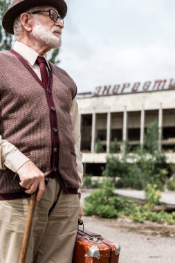 Pripyat, Ukrayna - 15 Ağustos 2019: Çernobil'de enerjik harflerle binanın yakınında bavul tutan kıdemli adam 