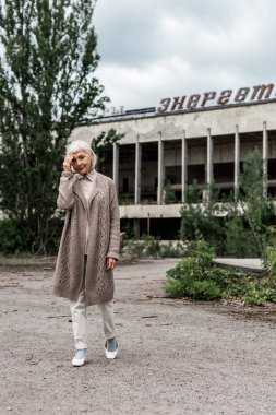 Pripyat, Ukrayna - 15 Ağustos 2019: Çernobil'de enerjik harflerle binanın yakınında yürüyen yaşlı kadın 