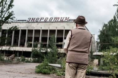 Pripyat, Ukrayna - 15 Ağustos 2019: çernobil enerjik yazı ile bina yakınında duran şapka emekli adam geri görünümü 