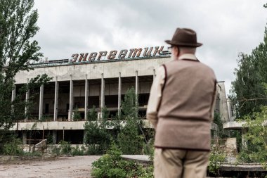 Pripyat, Ukrayna - 15 Ağustos 2019: Çernobil'de enerjik harflerle binanın yanında duran emekli adamın arka görünümü 