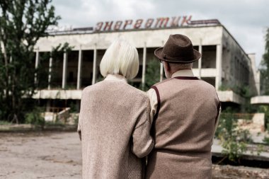 Pripyat, Ukrayna - 15 Ağustos 2019: Çernobil'de enerjik harflerle binanın yanında duran emekli erkek ve kadının arka görünümü 