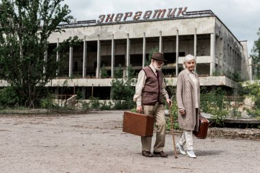 Pripyat, Ukrayna - 15 Ağustos 2019: Çernobil'de enerjik harflerle binanın yakınında bavulları olan emekli yolcular 