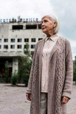 Pripyat, Ukrayna - 15 Ağustos 2019: Çernobil'de otel polissya yazısı ile binanın yakınında duran gri saçlı yaşlı kadın 