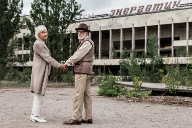 Pripyat, Ukrayna - 15 Ağustos 2019: Çernobil'de enerjik harflerle binanın yakınında el ele tutuşan emekli çift 