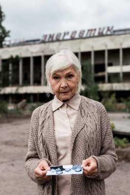 Pripyat, Ukrayna - 15 Ağustos 2019: Çernobil'de enerjik harflerle binanın yakınında fotoğraf tutan üst düzey kadın 