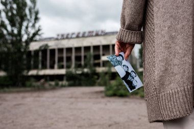 Pripyat, Ukrayna - 15 Ağustos 2019: Çernobil'deki binanın yakınında siyah beyaz fotoğraf tutan kıdemli kadının kırpılmış görünümü 