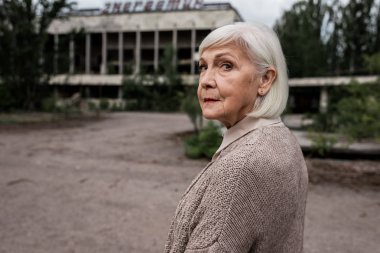Pripyat, Ukrayna - 15 Ağustos 2019: Üst düzey kadın Çernobil'de binanın yakınındaki kameraya bakıyor 
