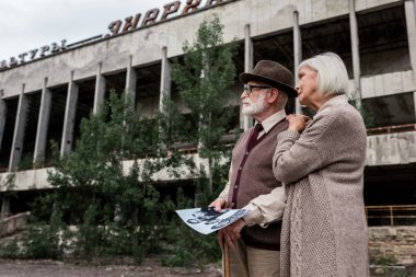 Pripyat, Ukrayna - 15 Ağustos 2019: Çernobil'de yazı ile binanın yakınında siyah beyaz fotoğraf tutan emekli erkek ve kadın 