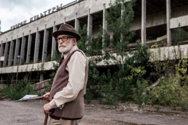 Pripyat, Ukrayna - 15 Ağustos 2019: Çernobil'deki binanın yakınında fotoğraf tutan kıdemli adam 