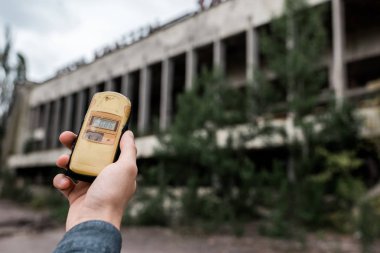 Pripyat, Ukrayna - 15 Ağustos 2019: Çernobil'deki binanın yakınında radyometre tutan adamın kırpılmış görünümü 