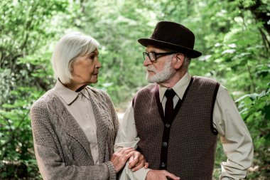 yeşil ağaçların yakınındaki kadına bakan gözlüklü yaşlı adam 