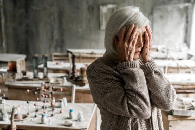 retired woman touching face and standing in dirty classroom  clipart