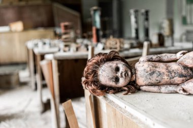 selective focus of creepy baby doll on wooden desk in classroom  clipart