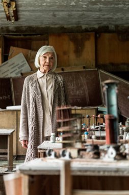 kirli terk edilmiş sınıfta duran emekli kadının seçici odak 