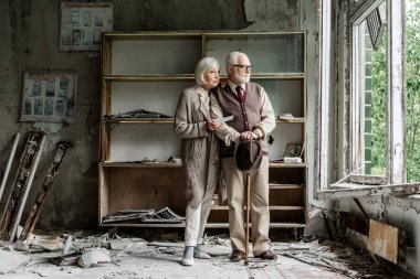 retired man and woman looking at window while standing in damaged classroom  clipart