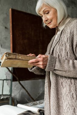 PRIPYAT, UKRAINE - AUGUST 15, 2019: retired woman with grey hair holding book in hands