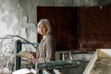 Pripyat, Ukrayna - 15 Ağustos 2019: tebeşir tahtasının yanında elinde kitap tutan gri saçlı emekli kadın