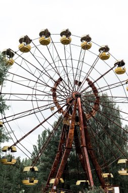 PRIPYAT, UKRAINE - AUGUST 15, 2019: abandoned and rusty carousel in amusement park with trees against sky  clipart