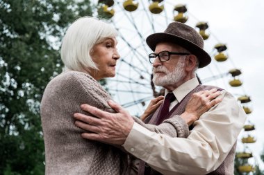 Pripyat, Ukrayna - 15 Ağustos 2019: Sakallı yaşlı adam lunaparkta dönme dolap yakınında emekli karısı ile sarılma