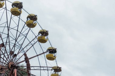 PRIPYAT, UKRAINE - AUGUST 15, 2019: abandoned and rusty ferris wheel in amusement park against blue sky with clouds  clipart
