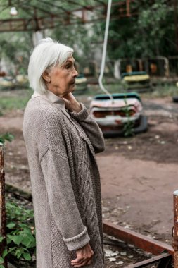 Pripyat, Ukrayna - 15 Ağustos 2019: terk edilmiş çarpışan arabaların yakınındaki lunaparkta duran kıdemli kadın 
