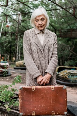 Pripyat, Ukrayna - 15 Ağustos 2019: lunaparkta bavul tutan üzgün yaşlı kadın 