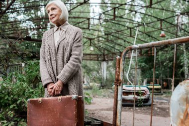 Pripyat, Ukrayna - 15 Ağustos 2019: lunaparkta bavul tutan kıdemli kadının seçici odak noktası 