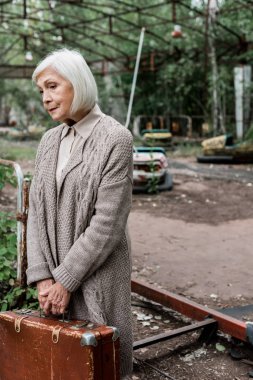 Pripyat, Ukrayna - 15 Ağustos 2019: lunaparkta bavul tutan yaşlı kadın üzgün 