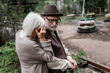 Pripyat, Ukrayna - 15 Ağustos 2019: şapkalı emekli kocasıyla ayakta duran yaşlı kadın üzgün 