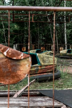 PRIPYAT, UKRAINE - AUGUST 15, 2019: selective focus of abandoned bumper cars in amusement park near metallic fence  clipart