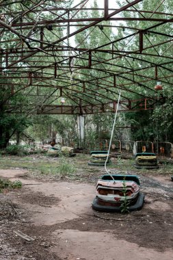 PRIPYAT, UKRAINE - AUGUST 15, 2019: bumper cars in abandoned amusement park near trees clipart