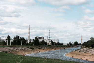 PRIPYAT, UKRAINE - AUGUST 15, 2019: abandoned chernobyl nuclear power plant near trees against blue sky  clipart