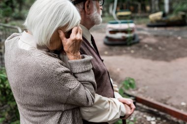 Pripyat, Ukrayna - 15 Ağustos 2019: Çernobil'deki lunaparkın yakınında hayal kırıklığına uğramış karısıyla ayakta duran yaşlı adamın kırpılmış görünümü 