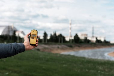 PRIPYAT, UKRAINE - AUGUST 15, 2019: cropped view of man holding radiometer near chernobyl nuclear power plant  clipart