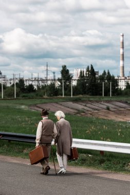 Pripyat, Ukrayna - 15 Ağustos 2019: Çernobil nükleer santrali yakınında bagajla yürüyen kıdemli çiftin geri görünümü 