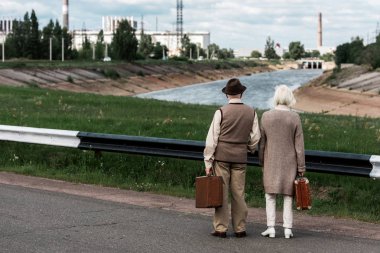 Pripyat, Ukrayna - 15 Ağustos 2019: Çernobil nükleer santrali yakınında bagajı olan kıdemli çiftin geri görünümü 