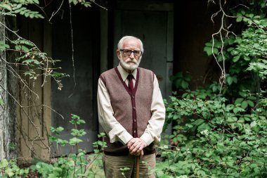 retired man in glasses standing with walking cane near house 