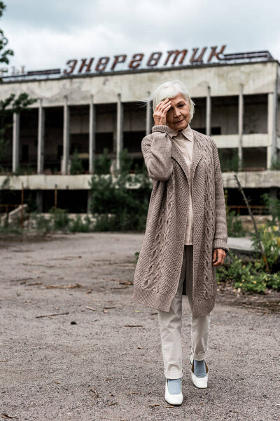 PRIPYAT, UKRAINE - AUGUST 15, 2019: senior woman walking near building with energetic lettering in chernobyl 