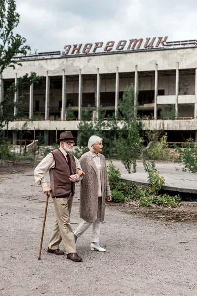 Pripyat, Ukrayna - 15 Ağustos 2019: Çernobil'de enerjik harflerle binanın yakınında yürüyen yaşlı çift 