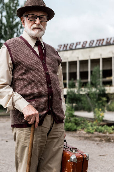 PRIPYAT, UKRAINE - AUGUST 15, 2019: retired man holding luggage near building with energetic lettering in chernobyl 