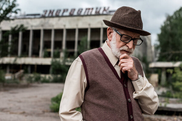 PRIPYAT, UKRAINE - AUGUST 15, 2019: pensive senior man standing near building with energetic lettering in chernobyl 