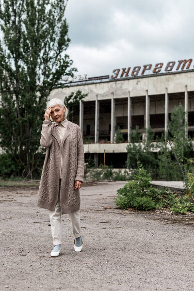 PRIPYAT, UKRAINE - AUGUST 15, 2019: senior woman walking near building with energetic lettering in chernobyl 