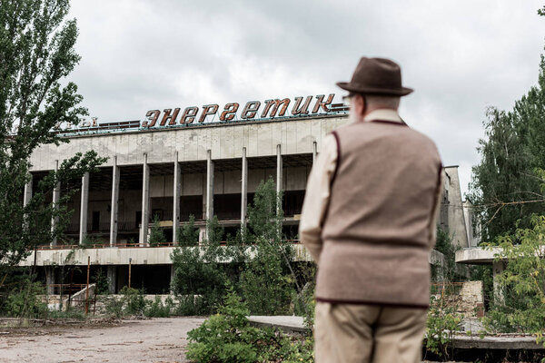 PRIPYAT, UKRAINE - AUGUST 15, 2019: back view of retired man standing near building with energetic lettering in chernobyl 