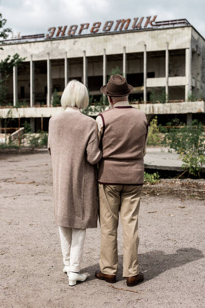 PRIPYAT, UKRAINE - AUGUST 15, 2019: back view of retired couple standing near building with energetic lettering in chernobyl 