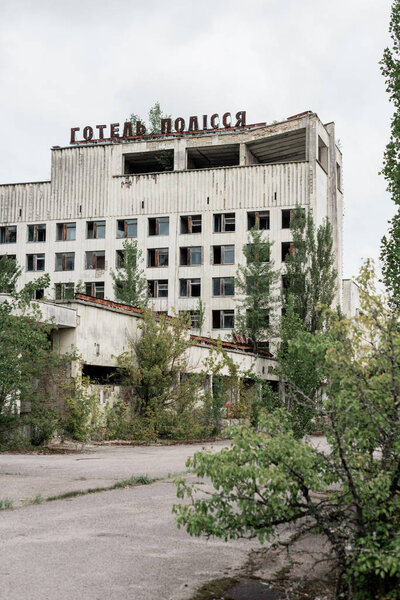 PRIPYAT, UKRAINE - AUGUST 15, 2019: building with hotel polissya letters near trees in chernobyl 