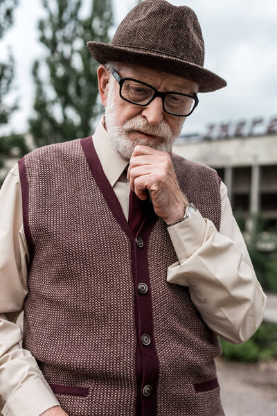 pensive senior man standing near building in chernobyl 